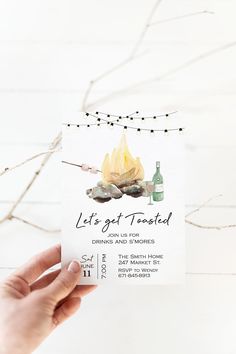 a person holding up a card with a campfire and bottle on it that says let's get toasted