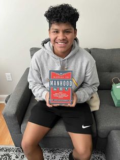 a person sitting on a couch with a book in their hand and smiling at the camera