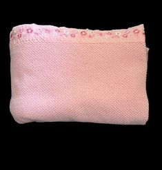 a pink and white pillow with flowers on the front, sitting against a black background