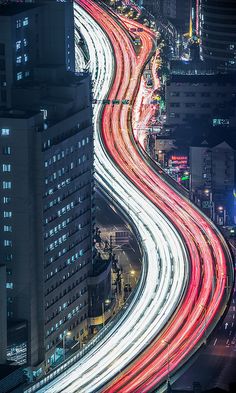 an aerial view of the city at night with long - exposure light trails in the foreground