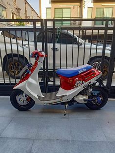 a red, white and blue scooter parked next to a fence