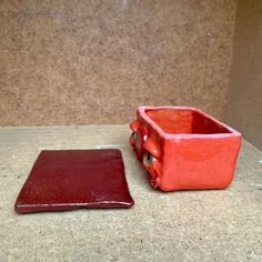 an orange and red container sitting on top of a counter next to a brown square