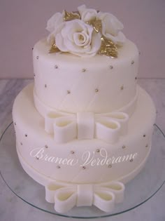 a three tiered cake with white flowers and bows on top is sitting on a glass platter