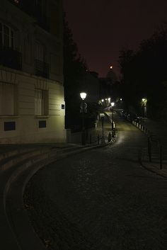 an empty street at night with lights on and steps leading up to the light pole