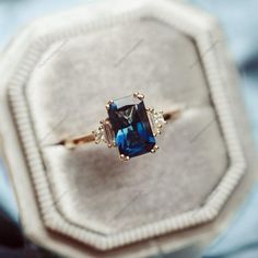 an engagement ring with a blue topazte surrounded by three diamond accents in a velvet box