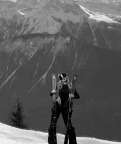 a woman standing on top of a snow covered slope holding skis