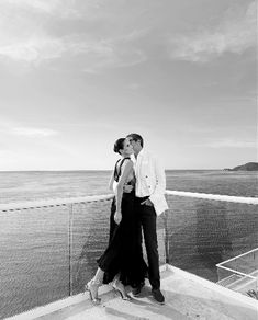 a man and woman kissing on top of a balcony next to the ocean in black and white