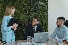 a group of people sitting around a table with laptops and papers in front of them