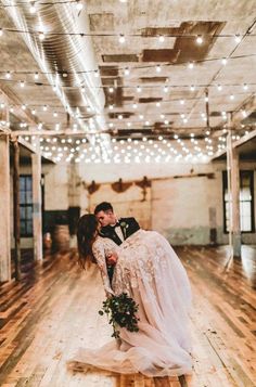 a bride and groom kissing on the dance floor in an old building with string lights