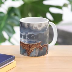 a coffee mug with a painting on it sitting on a table next to a book