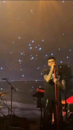 a man standing on top of a stage next to a keyboard and microphone in front of a star filled sky