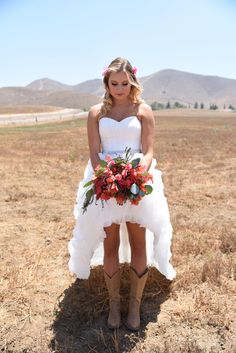 a woman in a wedding dress standing in a field with her bouquet on her knee