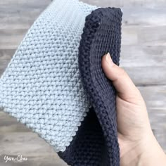 a hand is holding up a blue and white knitted pillow