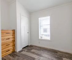 an empty room with white walls and wood flooring in the corner, next to a window