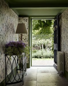 the hallway is decorated with wallpaper and floral designs, along with an iron planter filled with purple flowers