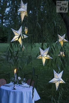 some paper stars hanging from a tree with lights on them and candles in the foreground