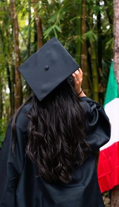 a woman wearing a graduation cap and gown standing in front of a forest filled with trees