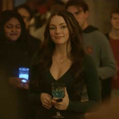 a woman holding a wine glass in front of her and people looking at the camera