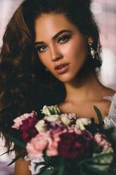 a woman holding a bouquet of flowers in her hand and looking at the camera with an intense look on her face