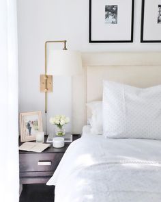 a white bed with two pictures on the wall above it and a lamp next to it