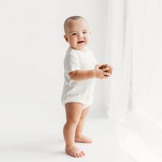 a smiling baby holding a donut in front of a white curtain with the light coming through it