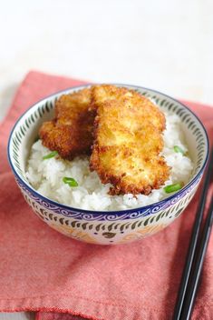 two fried meat patties on top of rice in a bowl with chopsticks