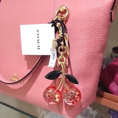 a pink handbag with two charms hanging from it's front and back handles