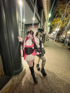 two people dressed in costumes standing next to each other on a sidewalk at night time