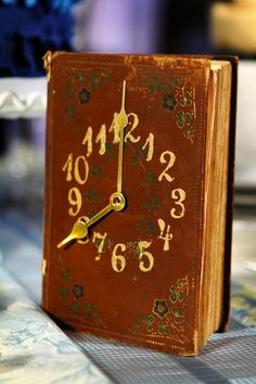 a clock made out of an old book sitting on a table with flowers in the background