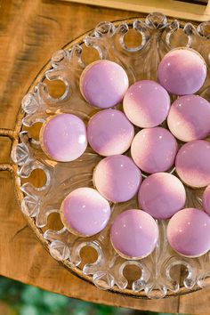 a glass plate filled with pink and white desserts on top of a wooden table