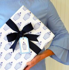 a woman holding a present wrapped in blue and white paper with a black bow on it