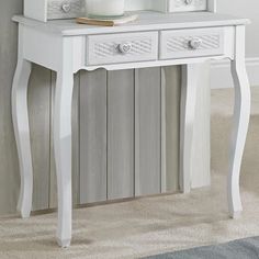 a white table with two drawers and a mirror on it's shelf next to a wall