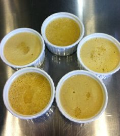 six cups filled with yellow liquid sitting on top of a metal countertop next to each other