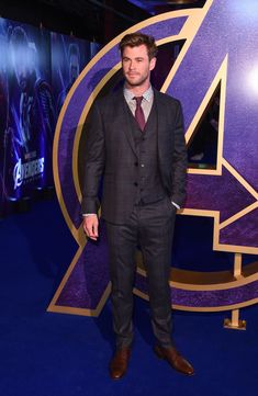 a man wearing a suit and tie standing in front of a avengers logo at an event