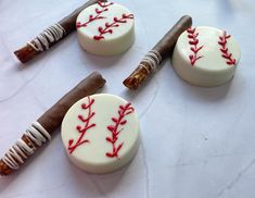 three baseball themed cookies are on a white tablecloth, with chocolate sticks sticking out of them