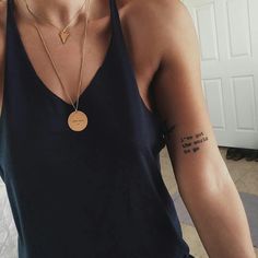 a woman wearing a black tank top with a gold disc pendant on her left arm