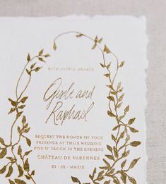 the wedding card is decorated with gold foil leaves and vines, which are on top of a white piece of paper