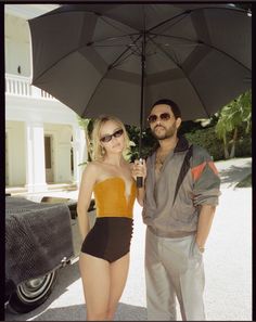 a man standing next to a woman in a bathing suit and holding an open umbrella