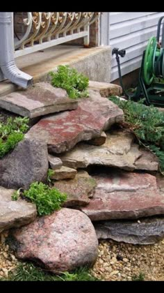 a garden with rocks and plants on the ground next to a porch area in front of a house