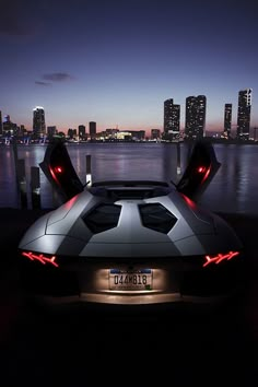 the back end of a sports car parked in front of a body of water at night