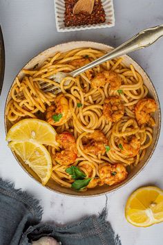 a bowl filled with pasta and shrimp next to lemon wedges, seasoning and spices