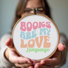 a woman holding up a cross - stitch hoop that says books are my love language