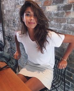 a woman sitting at a table in front of a brick wall with her legs crossed