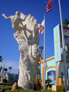 there is a statue in front of a building with flags flying from it's sides