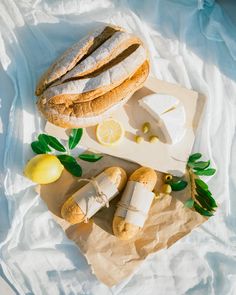 bread, cheese and lemons are on a cutting board with some leaves next to it