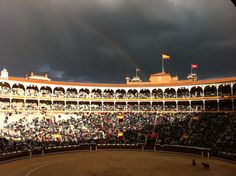 an arena full of people with a rainbow in the sky over them and dark clouds