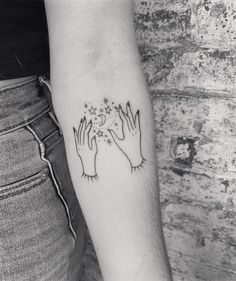 two hands holding stars and moon tattoo on the left inner arm, black and white