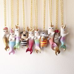 a row of ceramic mermaid cats hanging from gold chain necklaces on a white wall