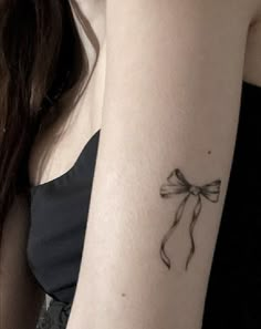 a woman's arm with a bow tattoo on the left side of her arm