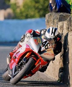 a person riding a motorcycle on a race track next to a stone wall and bushes